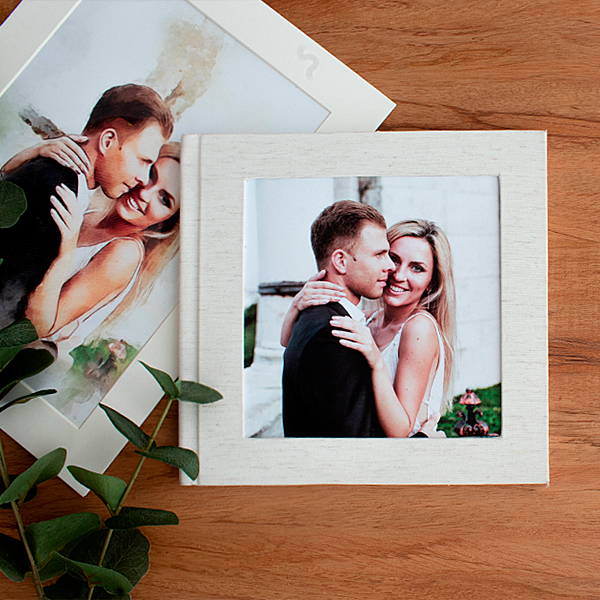 A versatile linen layflat photo album featuring a couple's wedding photo is displayed on a wooden surface, with additional prints in the background. This handmade photo book, created by an online photo book maker, FlipChap is ideal for preserving cherished memories from weddings, boudoirs, and other special occasions.